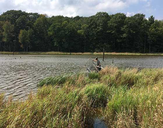 Student demonstrating wildlife research equipment in a pond